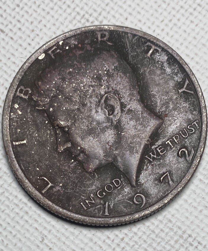 1972 Kennedy half dollar missing clad layer error showing reddish-orange copper surface where nickel cladding is absent compared to normal silver-gray surface
